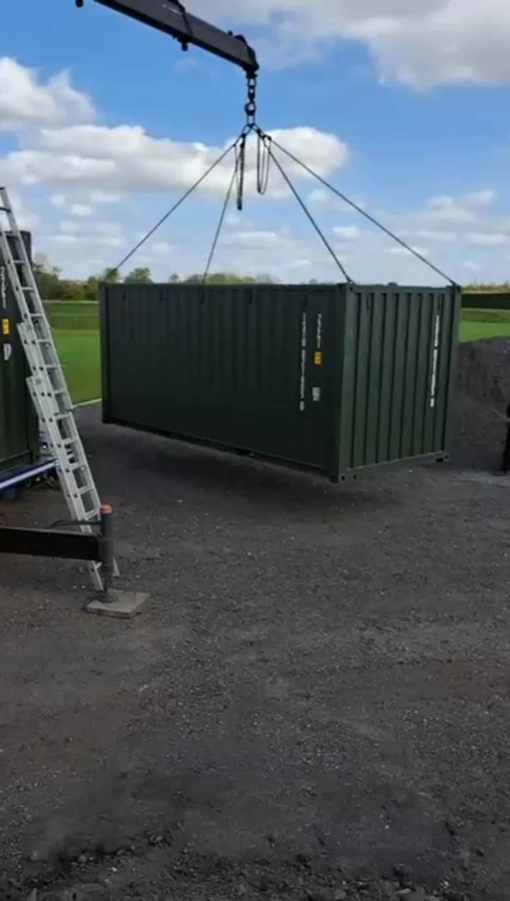 Crane placing a green shipping container onto prepared ground
